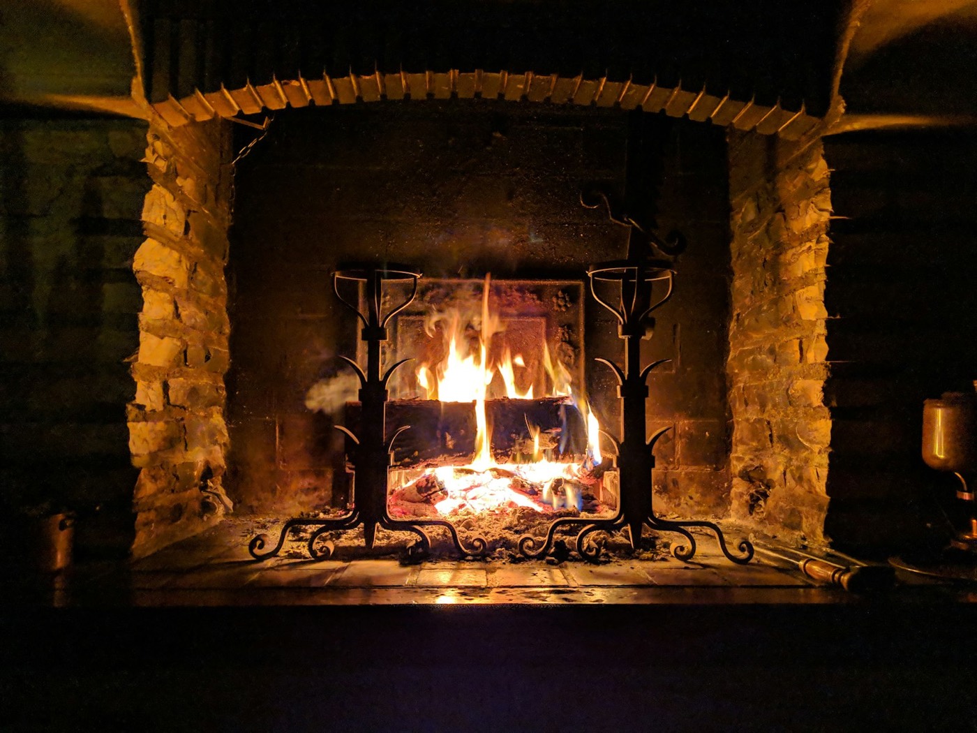 Grande cheminée ancienne en pierre avec feu de bois et chenets en fer forgé